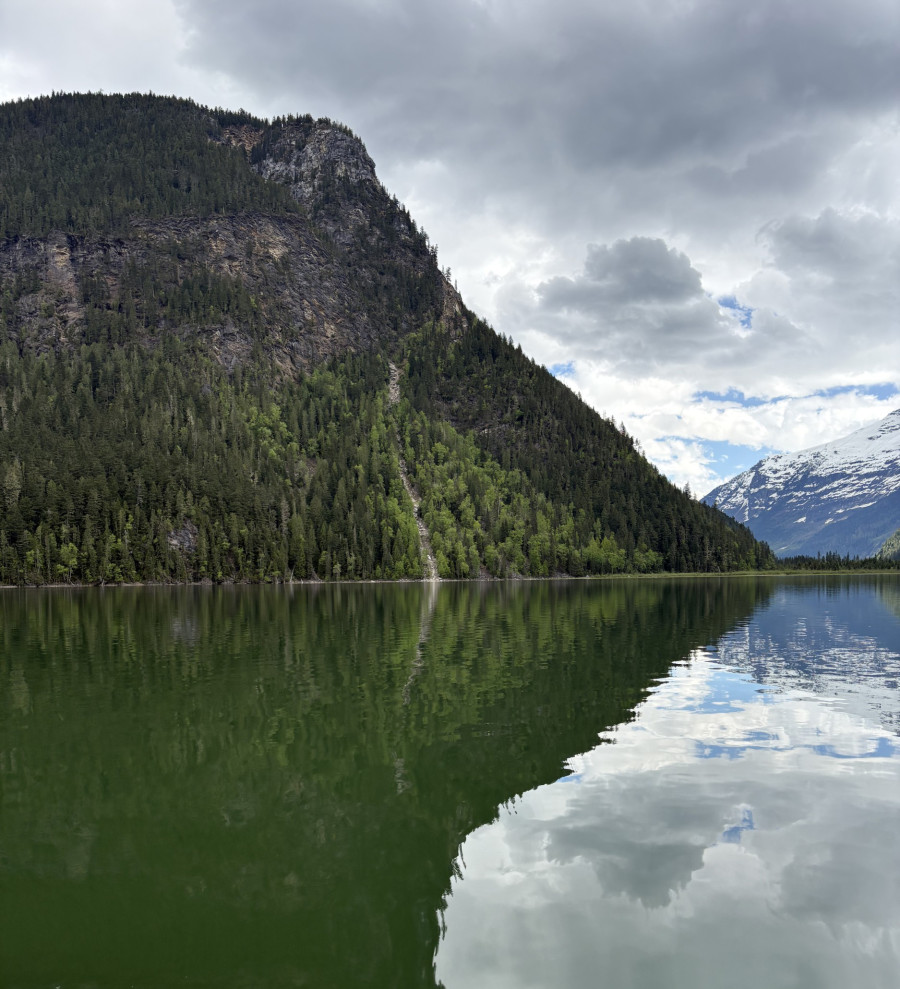 Ein See in dem sich ein Berg im Hintergrund spiegelt, bewölkt.